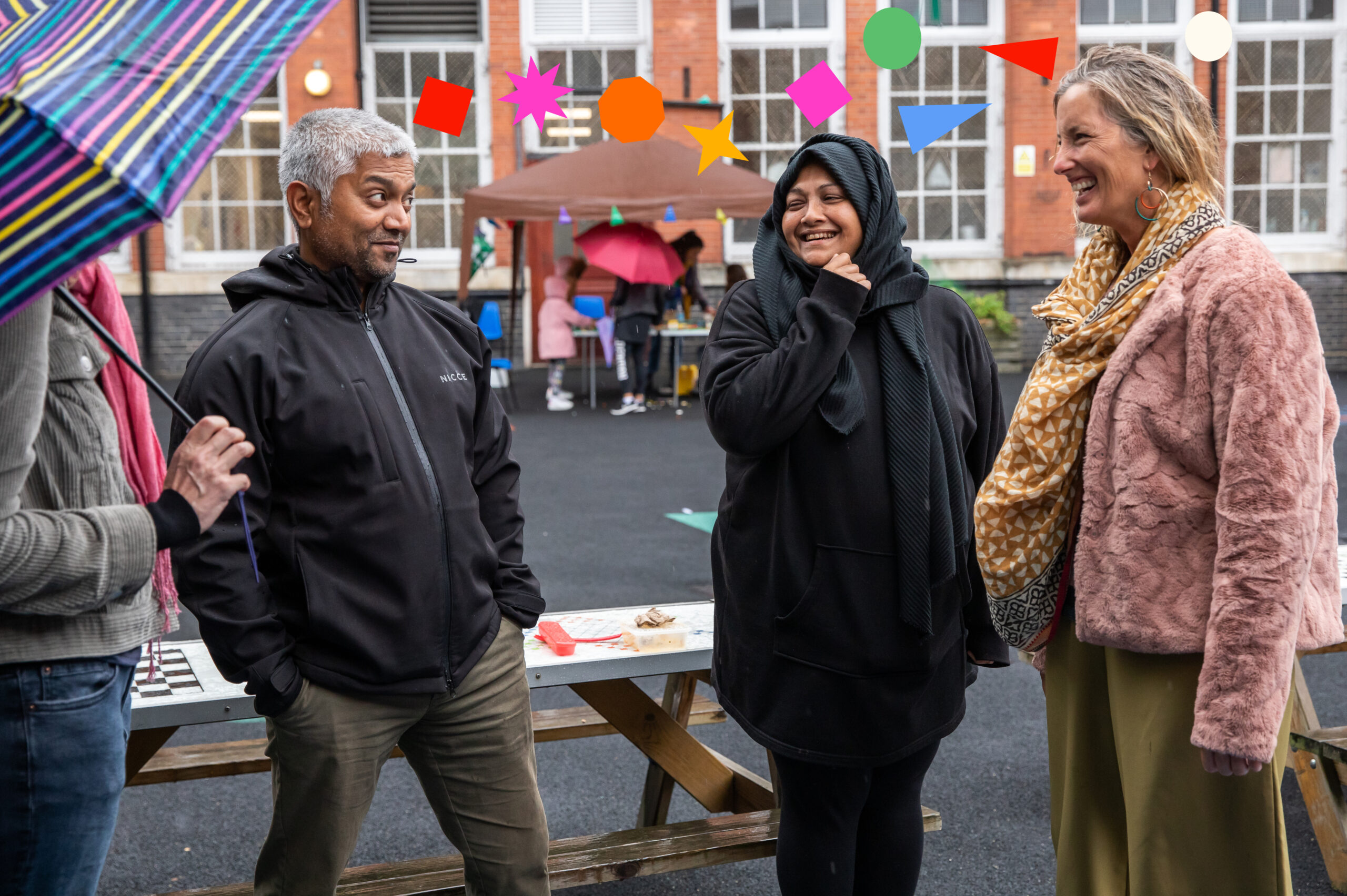 A group of four adults gather in a school playground chatting and smiling. Colourful 2D shape overlays form a line between their heads.