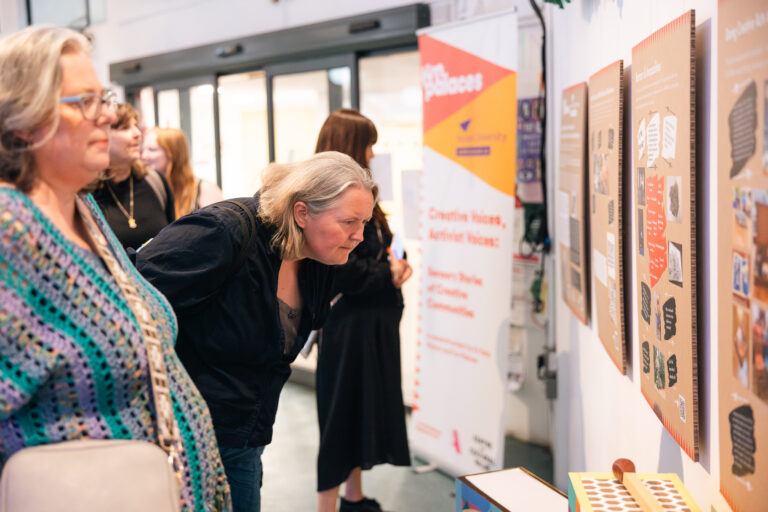 Visitors look closely at the Creative Voices, Activist Voices exhibition boards in a bright foyer.