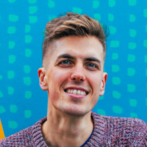 Alex Marshall, Marketing and Communications Manager for Fun Palaces, in front of a colourful blue mural.