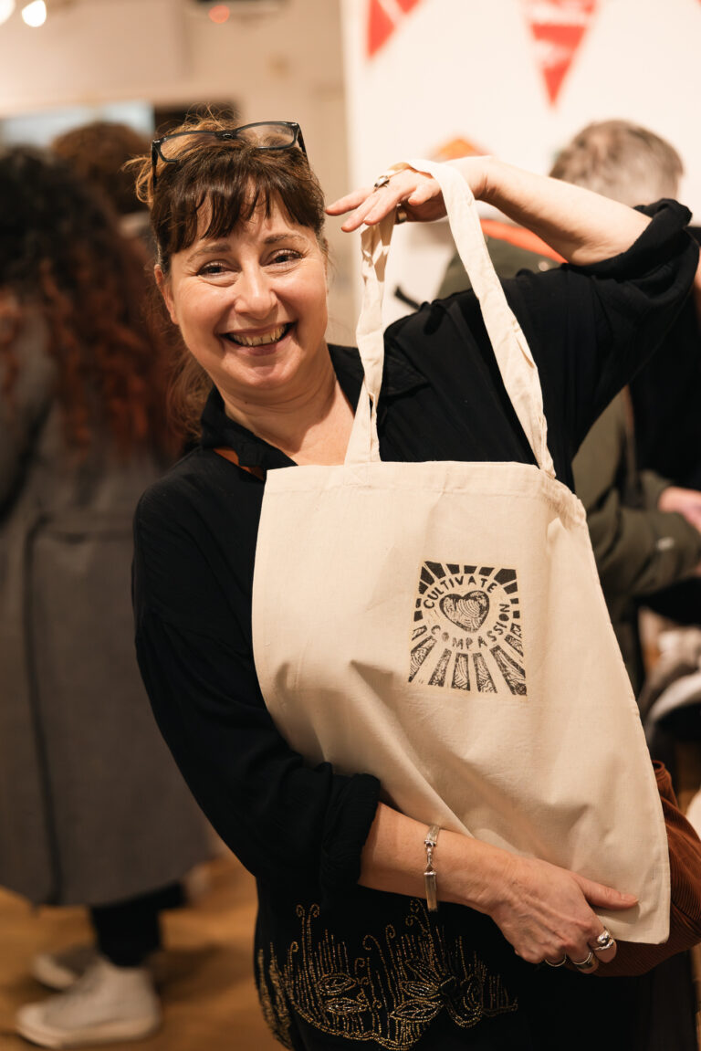 A woman smiling broadly as she holds up a Fun Palaces tote bag printed with a hand-drawn logo.