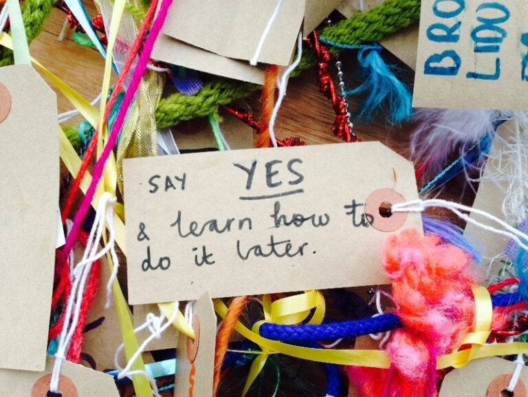 Handwritten luggage tags tied with ribbon and wool, one reading "Say yes and learn how to do it later".