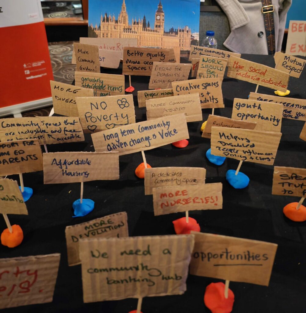 Photo of mini protest placards. Some read: long term community driven change and voice, no poverty, affordable housing, more nurseries, work should be fun, and more.