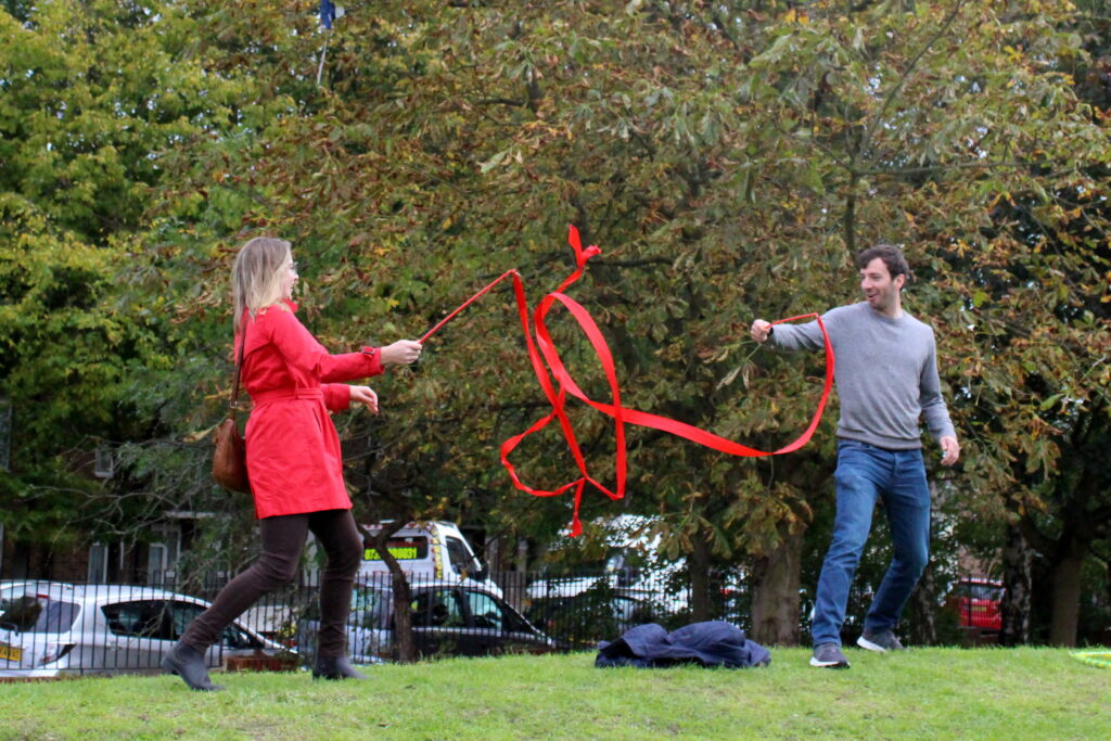 picture of a women in a red jacket and a man in a grey sweatshirt and jeans, having fun using rhythmic gymnastics ribbons