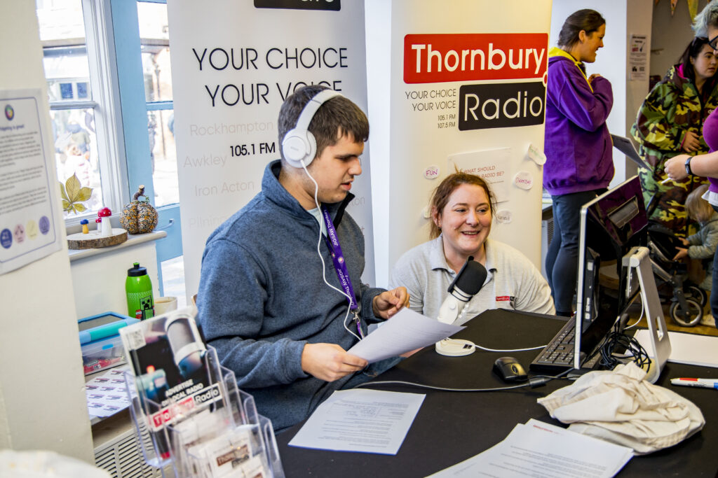 Picture of two people speaking on the radio. In the background are two pop-up banners reading your choice, your voice and thornbury radio.