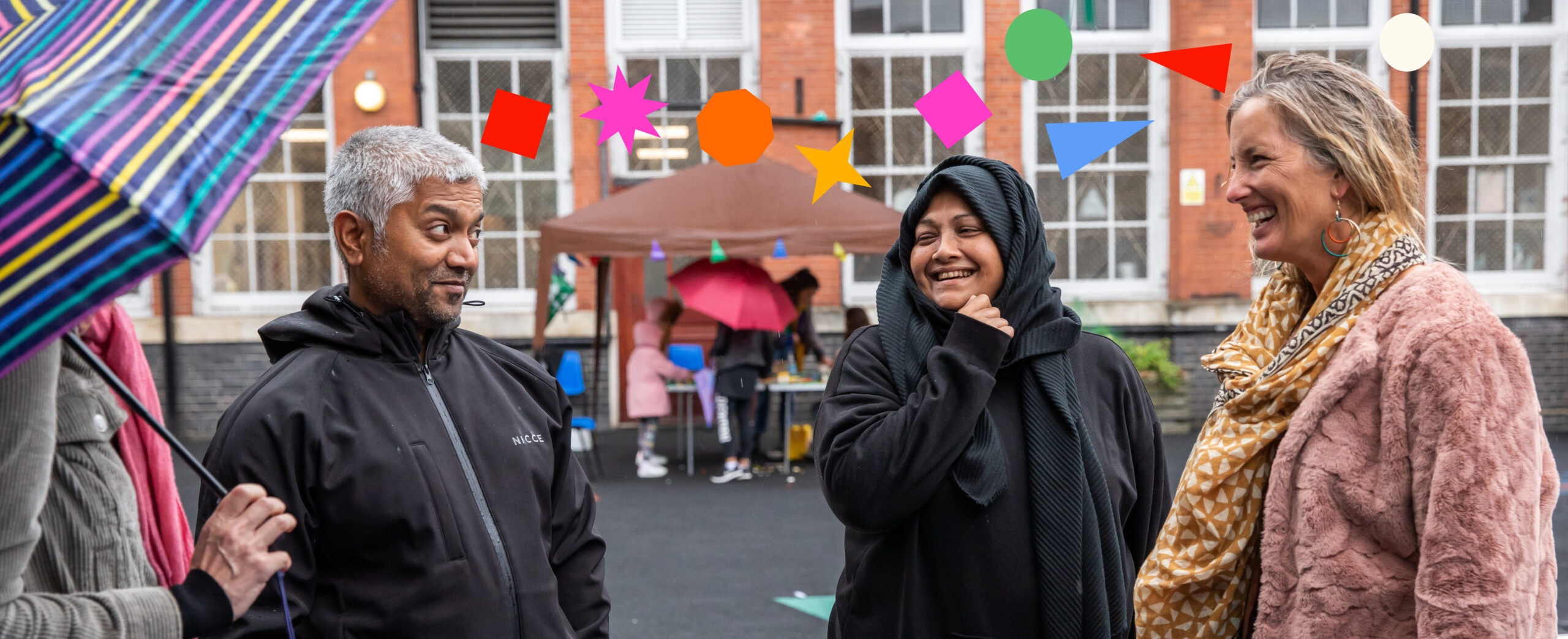  A group of four adults gather in a school playground chatting and smiling. Colourful 2D shape overlays form a line between their heads.