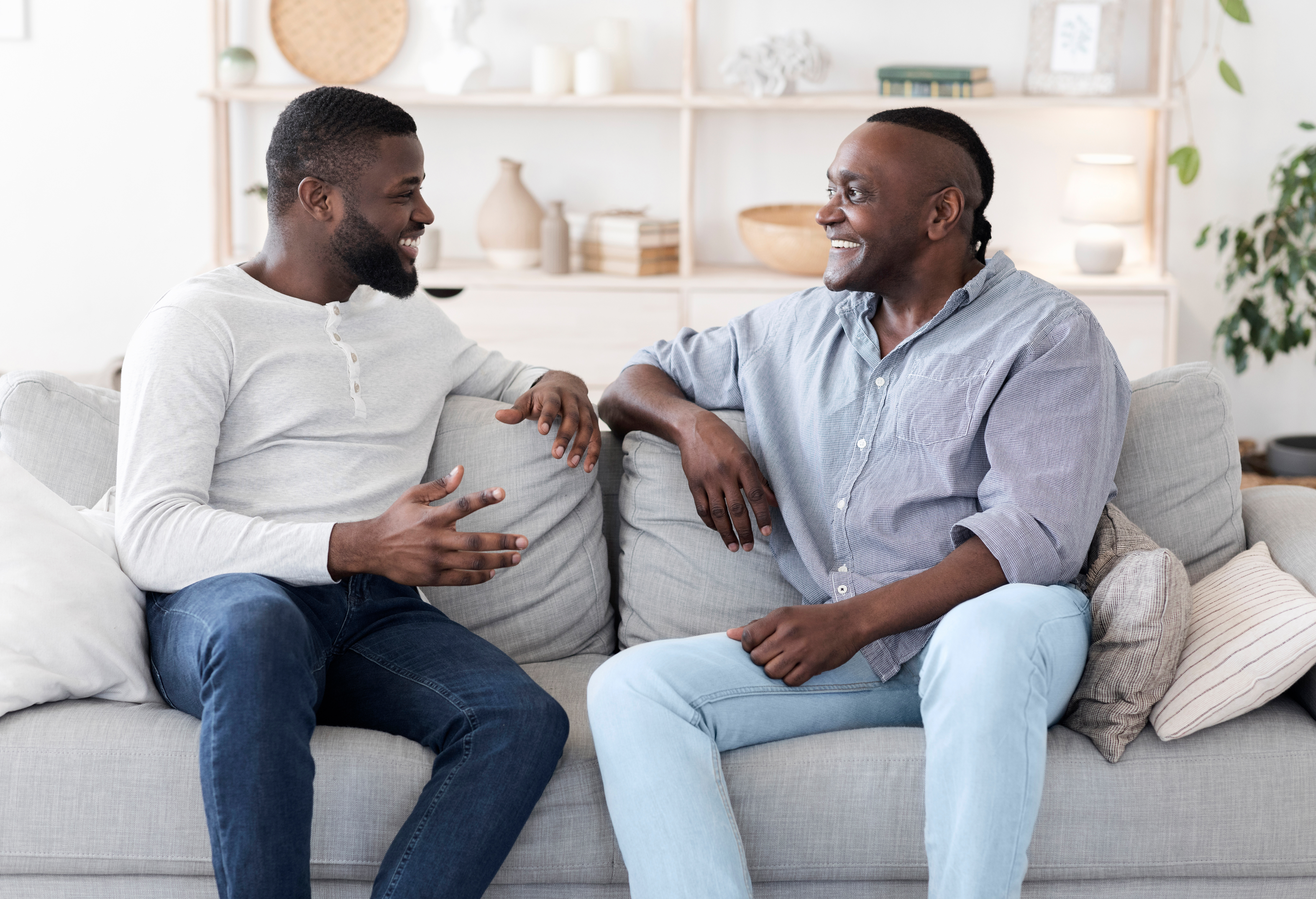 Two Black men, one young, one older, chatting happily on a sofa
