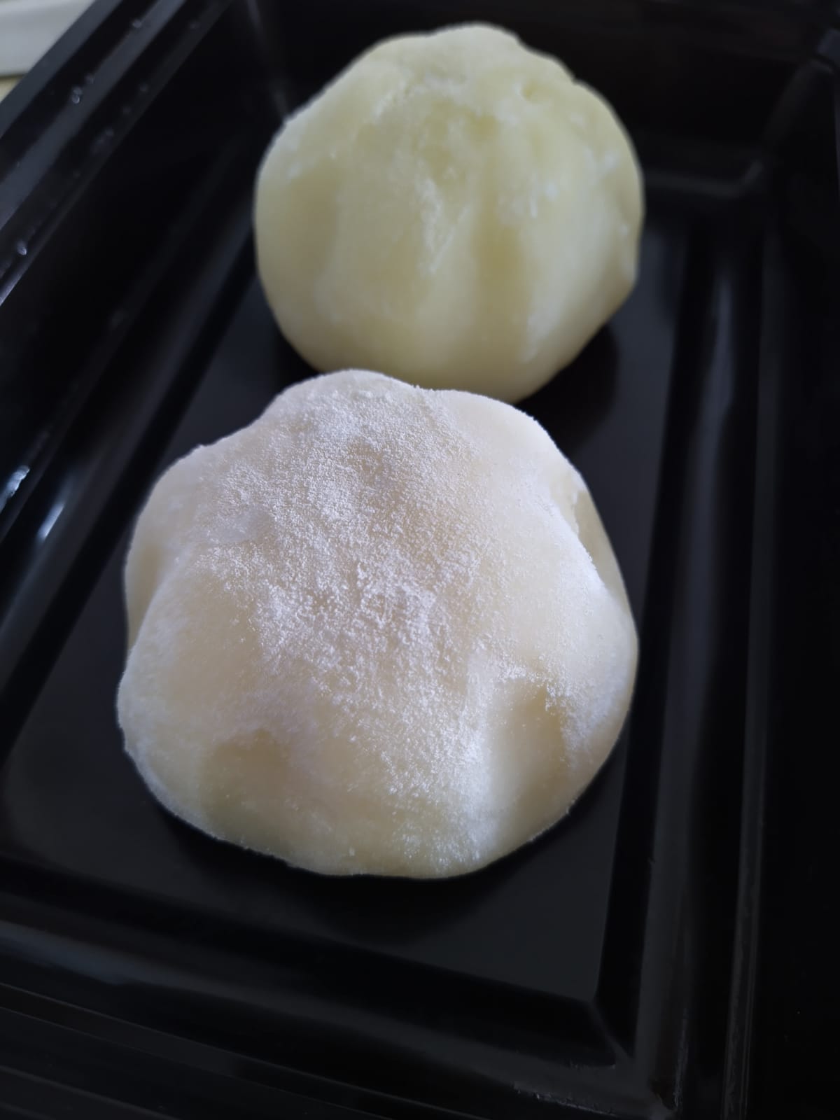 Two white snow skin moon cakes, made by Jasmine, placed on a black contained
